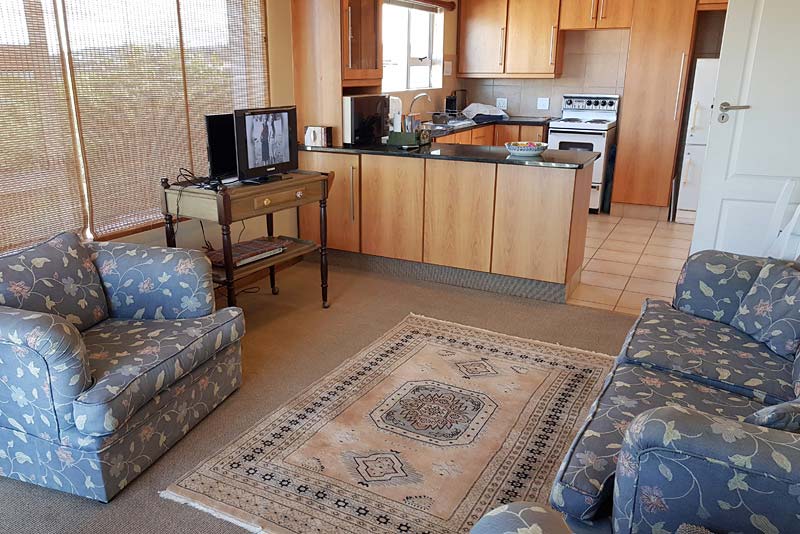 Small sitting room, with entry from outside, with view of fully equipped kitchen 